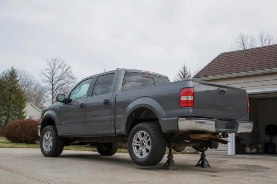 Gray pickup on jack stands with orange scale rust along rear frame rail